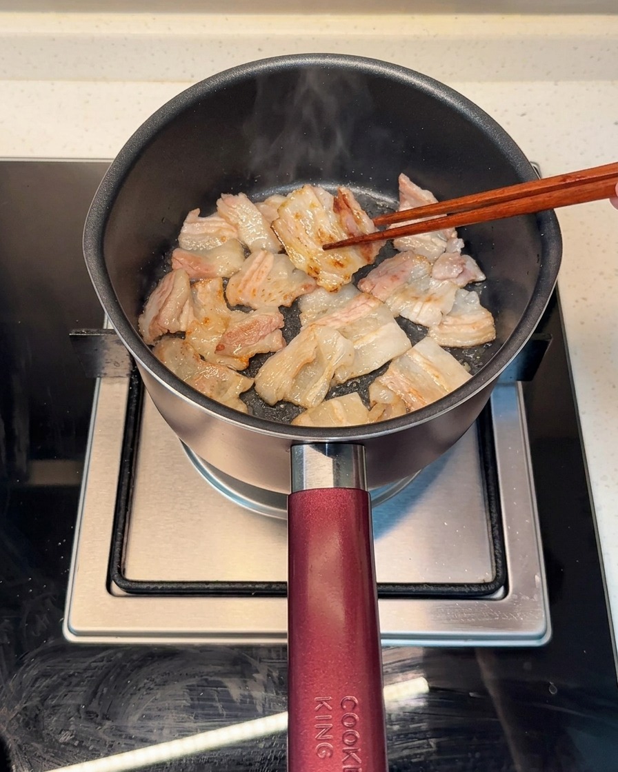 鍋で豚バラ肉を両面こんがりと焼いている様子。脂が溶け出している。
