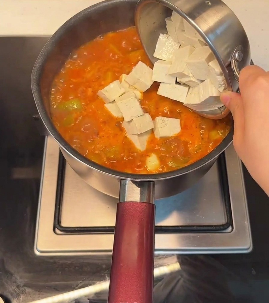 沸騰している赤いスープの中に、角切り豆腐を入れている様子。