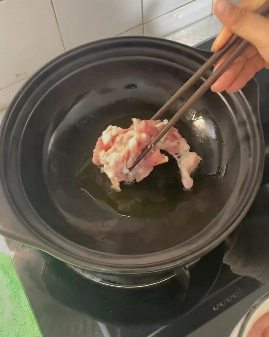 箸を使って熱した土鍋に豚バラ肉を入れる様子。
