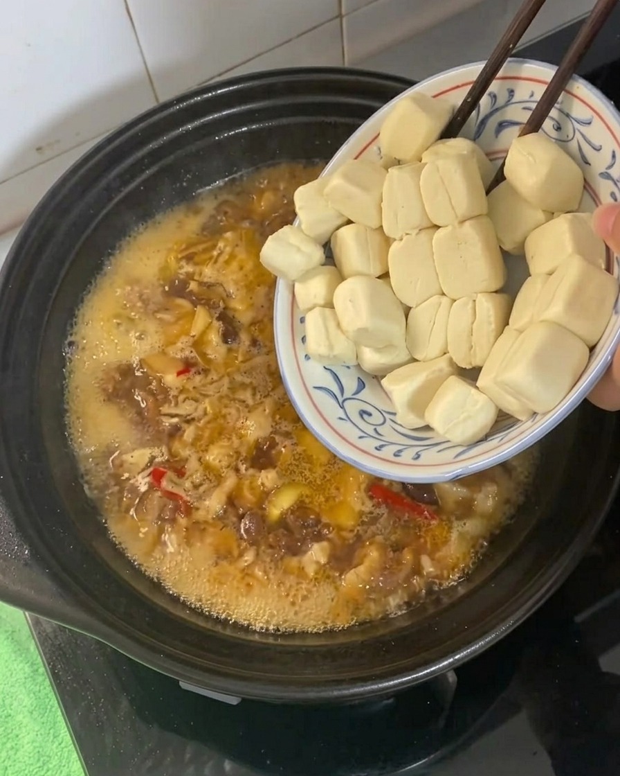 ぐつぐつと煮える黄金色のスープに豆腐を入れる様子。