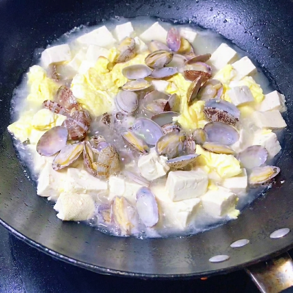 あさり、豆腐、卵の煮込みに葉野菜を加えて仕上げている様子。