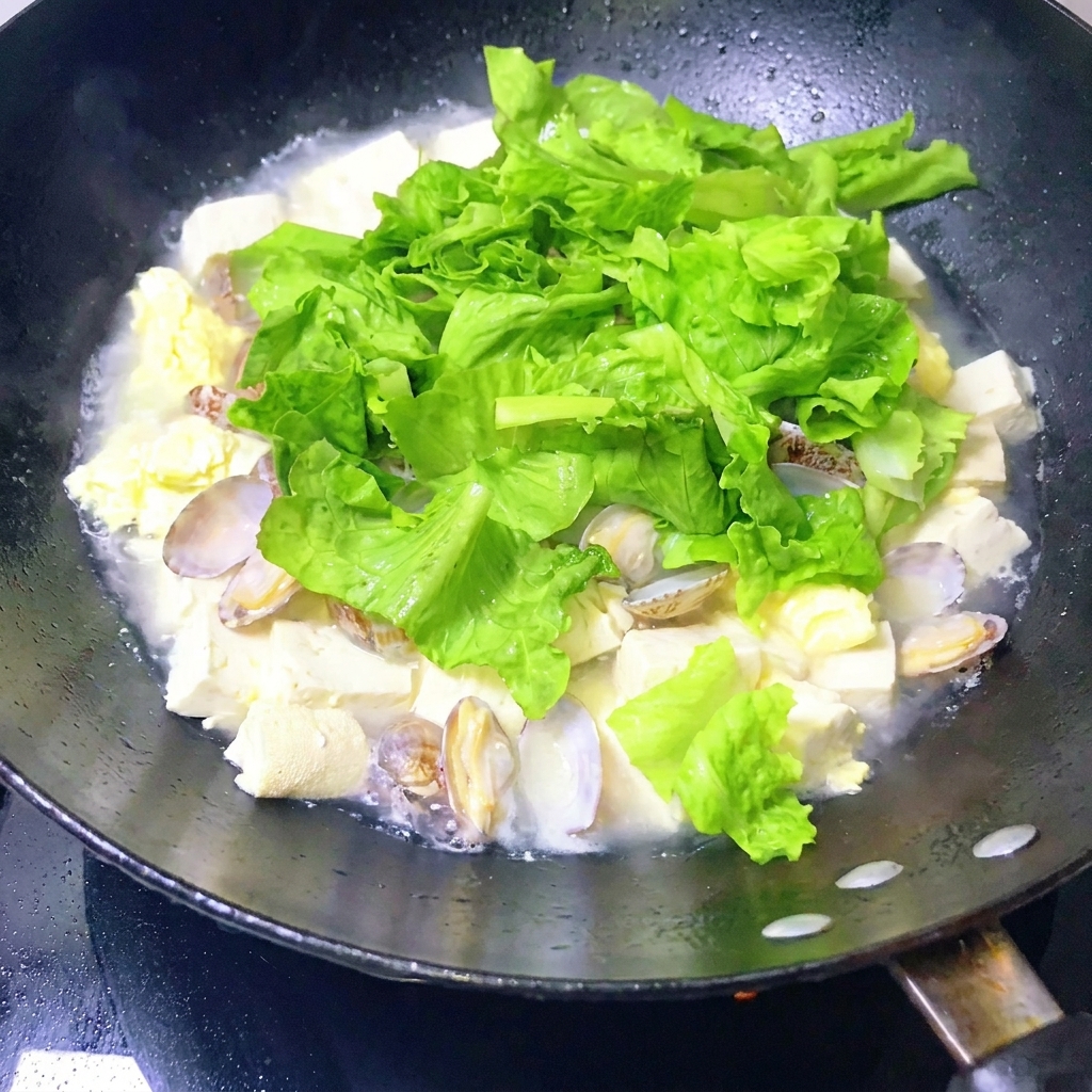 完成したあさりと豆腐の煮込みをお玉で軽く混ぜている様子。