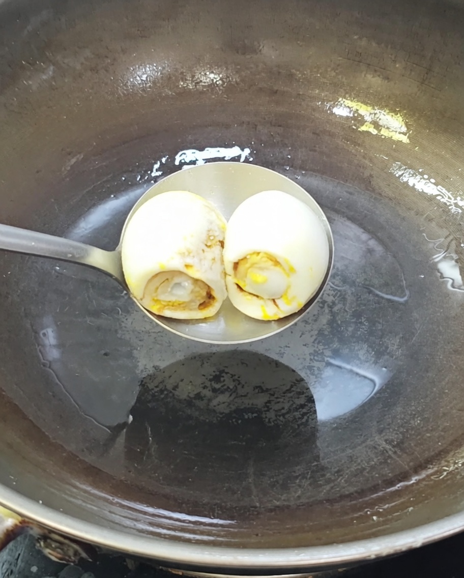 熱した中華鍋で油と一緒に炒められる2個の塩漬けアヒルの卵。