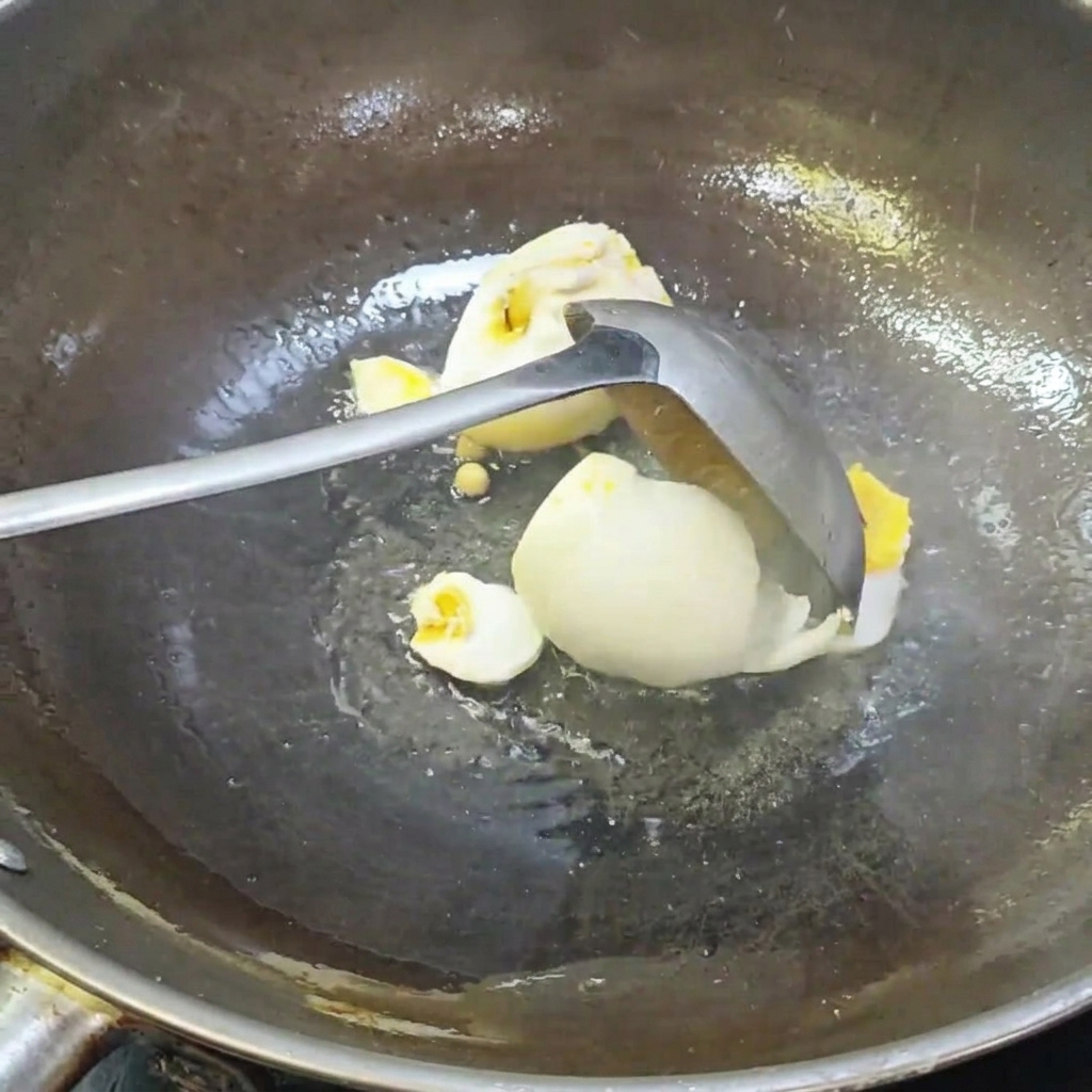 お玉で中華鍋の中の塩漬け卵を崩している様子。
