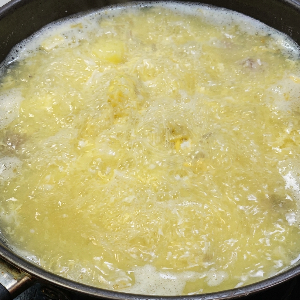 煮立っている豆腐と塩卵のスープに塩とホワイトペッパーで味付けをしている様子。
