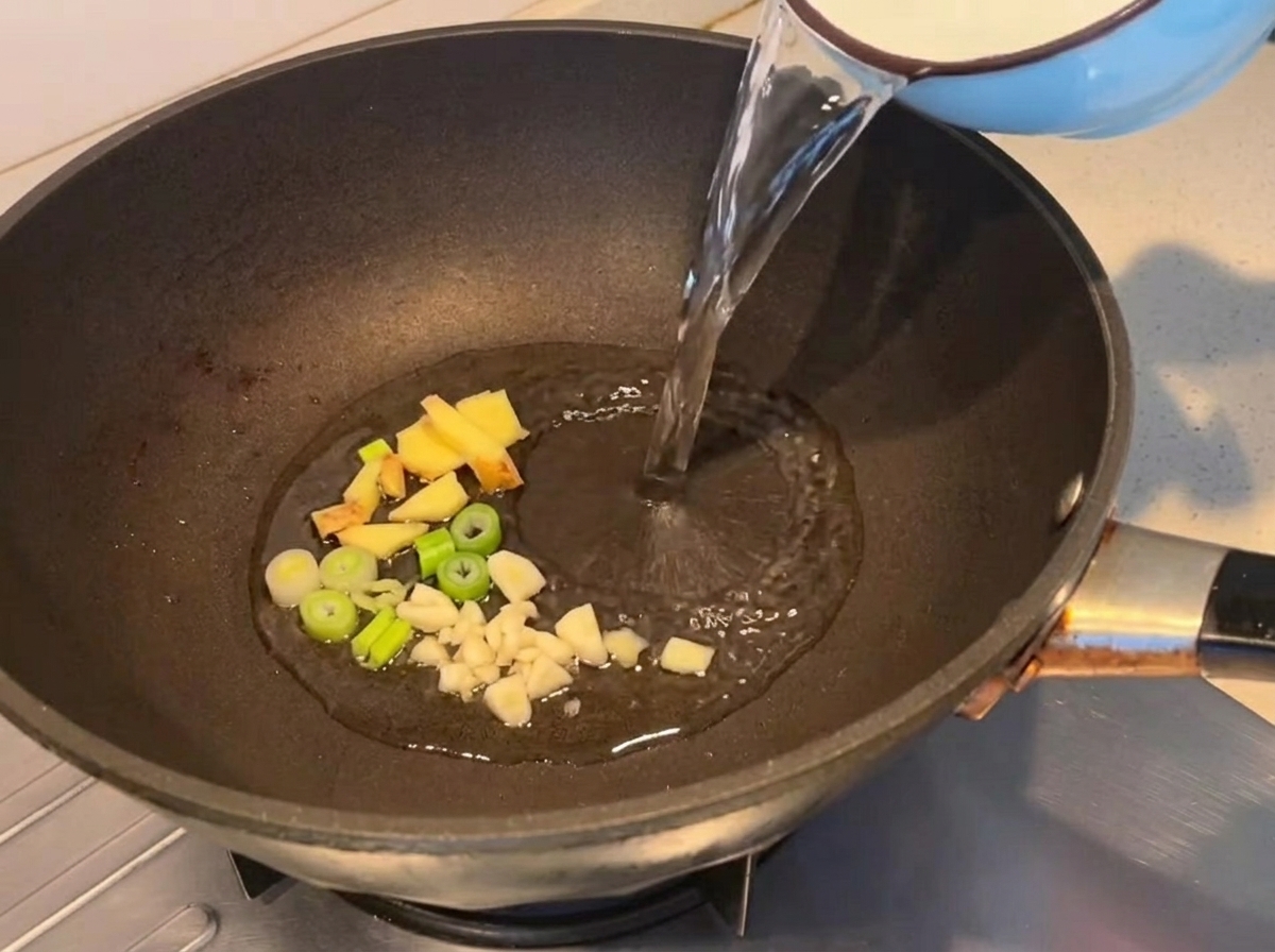 鍋で生姜と長ねぎを炒め、水を入れている様子。