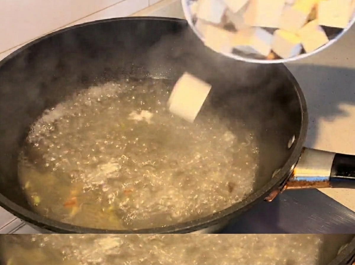 煮立ったスープにあさりと豆腐を入れている様子。