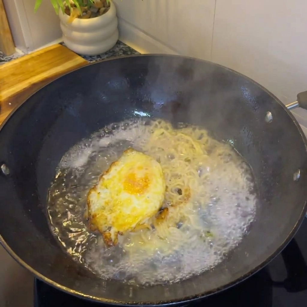 卵とネギが入ったフライパンに熱湯を注ぐ様子。