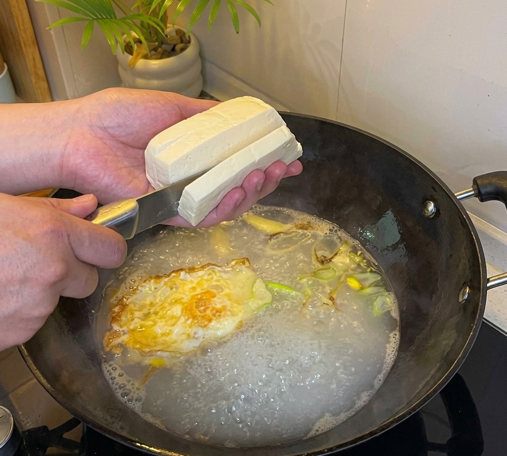 煮立っているスープに豆腐を小さく切って加えている様子。