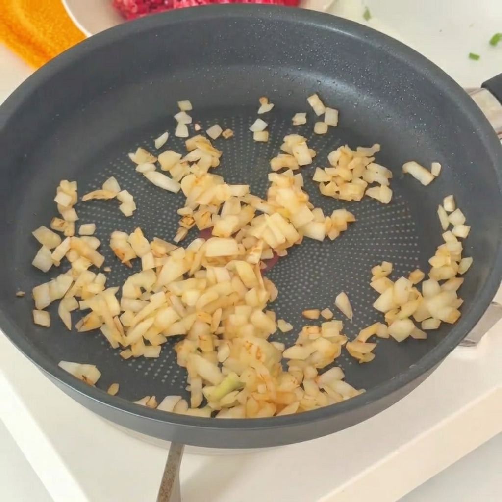 ボウルに入れた生の牛ひき肉に、炒めた玉ねぎを加える様子。