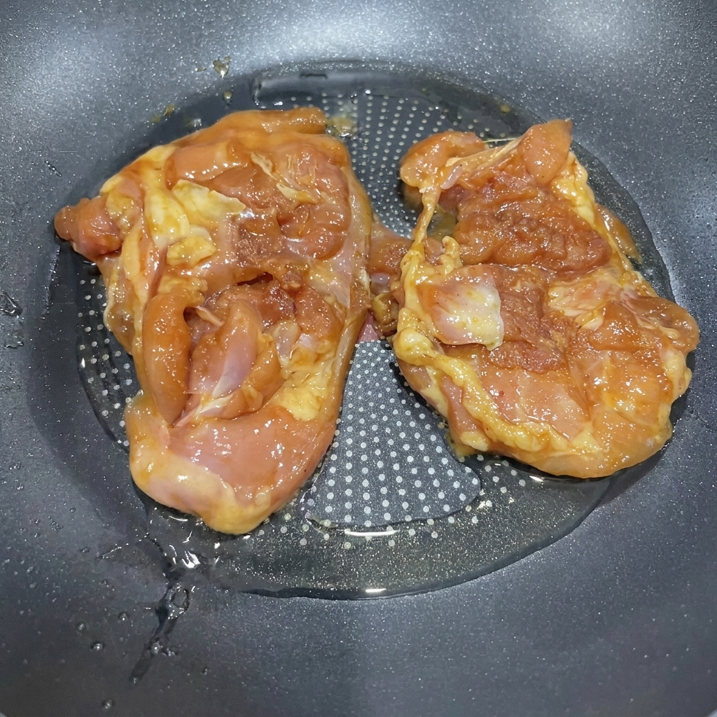 フライパンで油を熱し、照り焼きソースに漬けた鶏肉を焼いている様子。