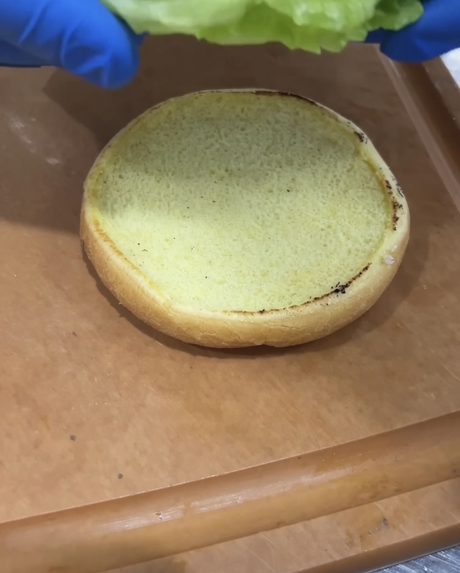 焼いたバンズの上にレタスとスライストマトを乗せている様子。