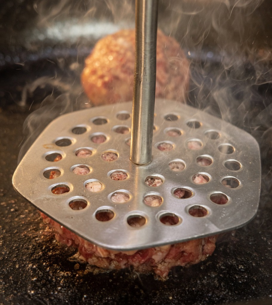 ミートプレスを使って、熱いフライパンの中で肉ボールを平らに押しつぶしている様子。