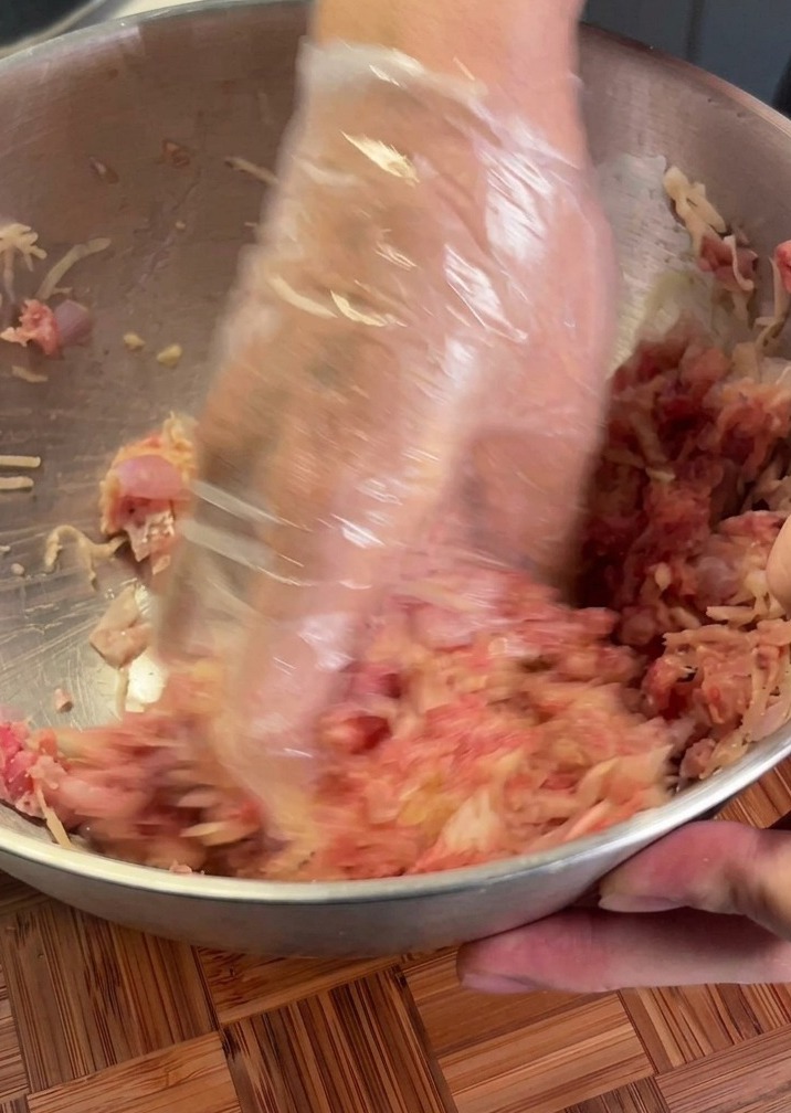 手袋をした手で、ひき肉とジャガイモをボウルで混ぜている様子