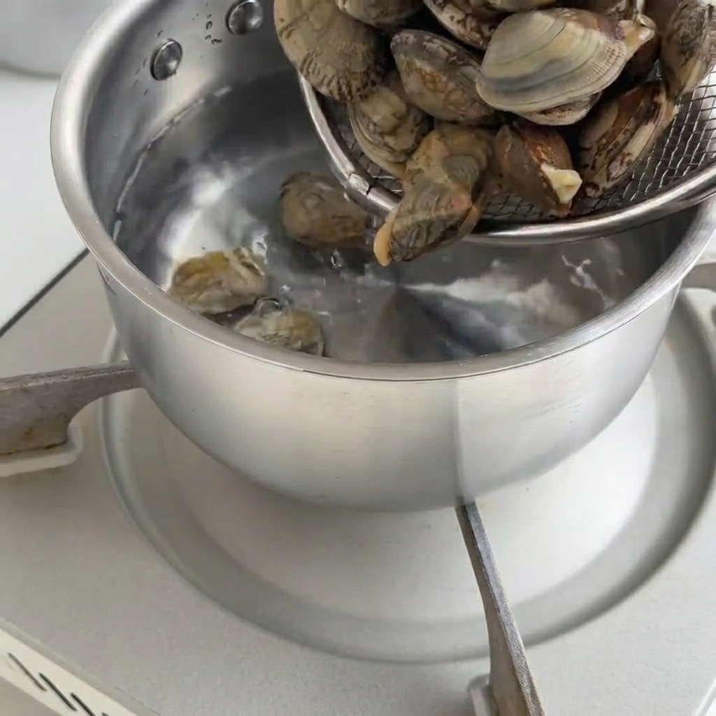 鍋の中で殻が開くまで茹でられている新鮮なアサリ。