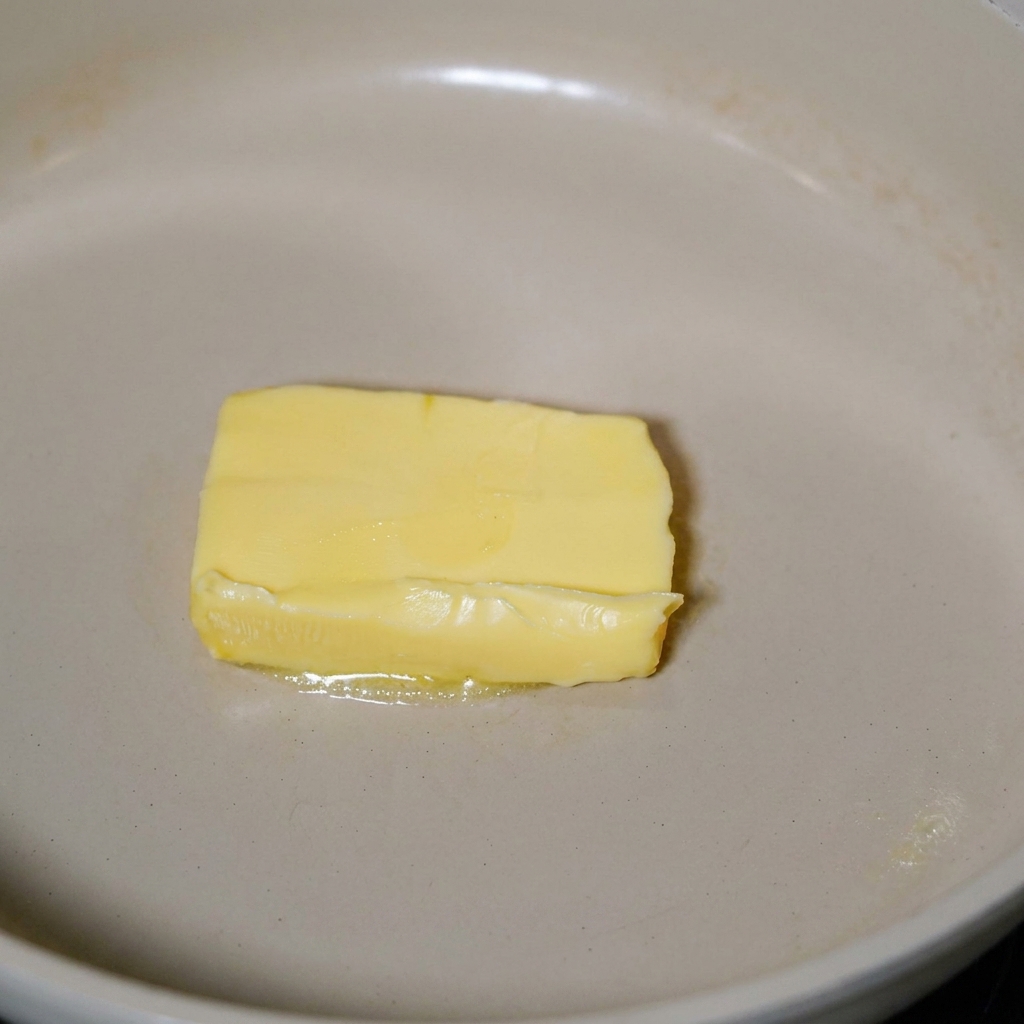 フライパンで溶けたバターの中を炒められているベーコン。