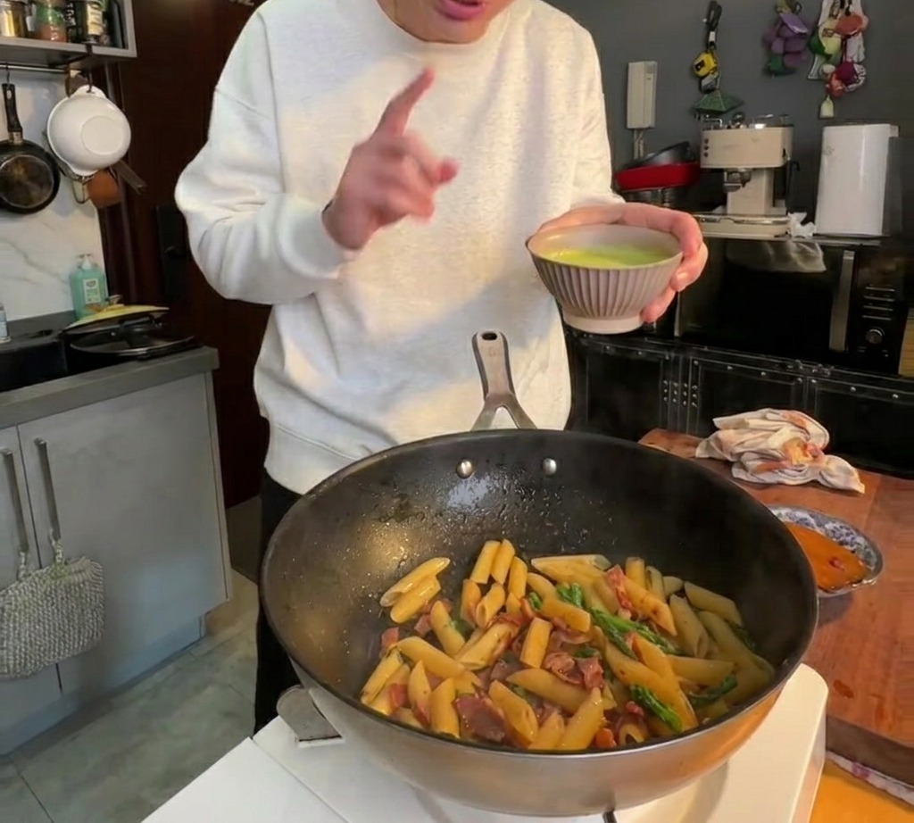 ペンネの上から滑らかな緑のアスパラソースが注がれ、全体が綺麗に和えられている様子。