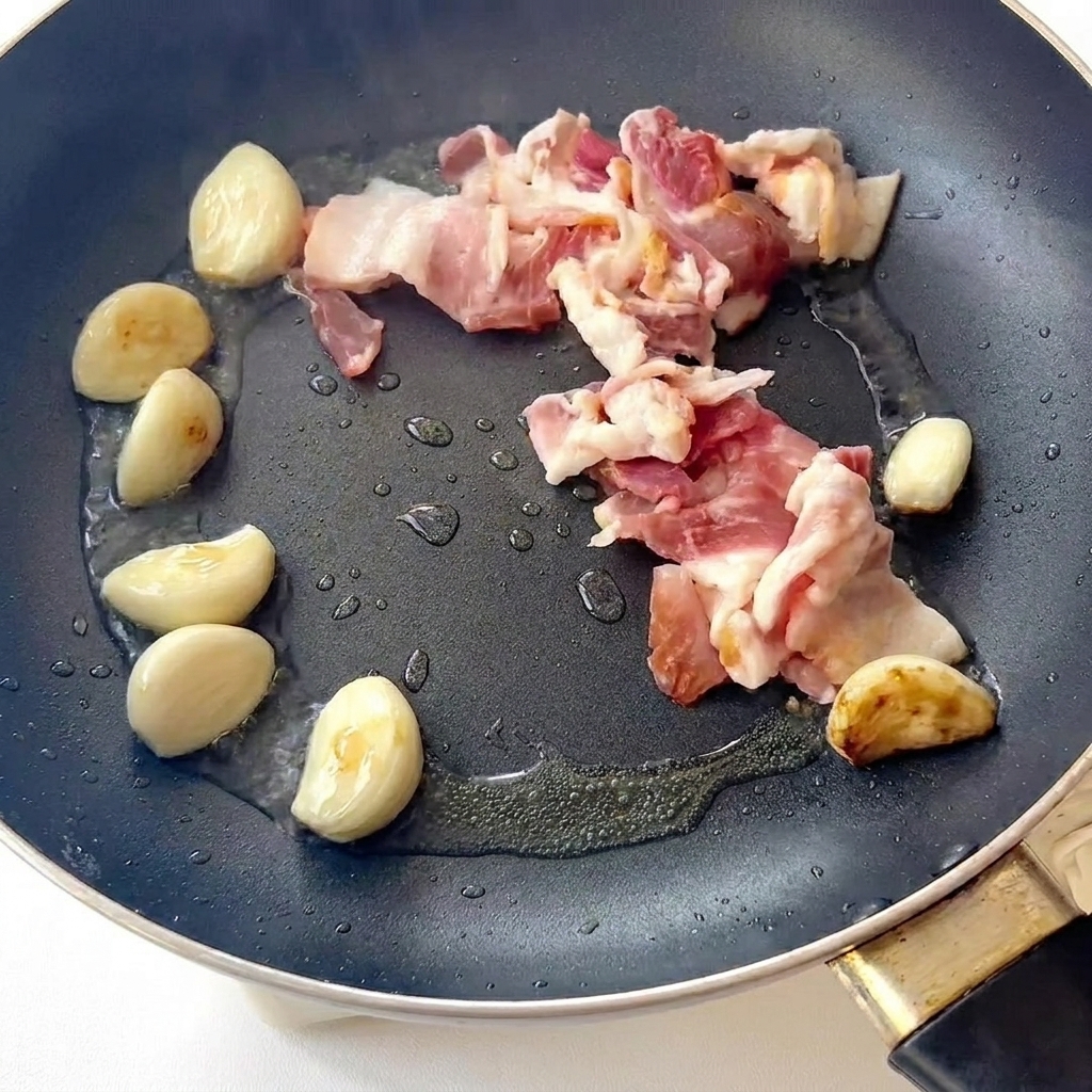 フライパンでベーコンとにんにくを炒めている様子。