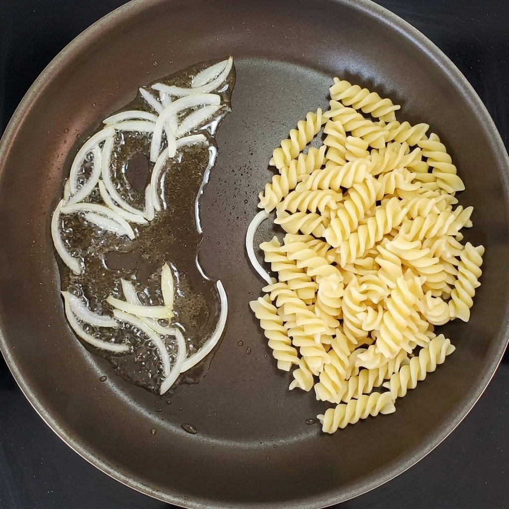 炒めた玉ねぎに茹でたパスタを合わせている様子