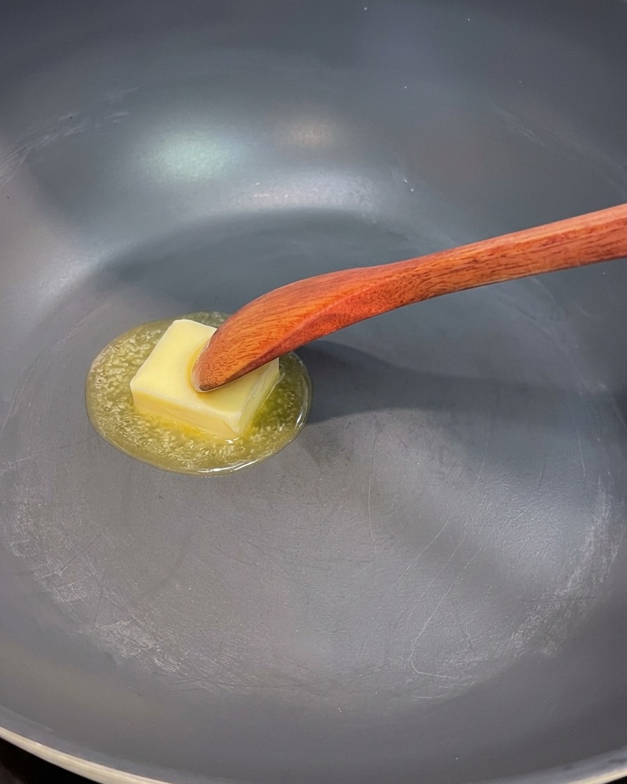 フライパンでバターを溶かし、玉ねぎ、きのこ、アスパラを炒めている様子。