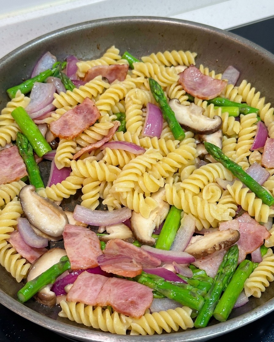 パスタと具材をフライパンで合わせ、醤油と黒胡椒で味付けしている様子。
