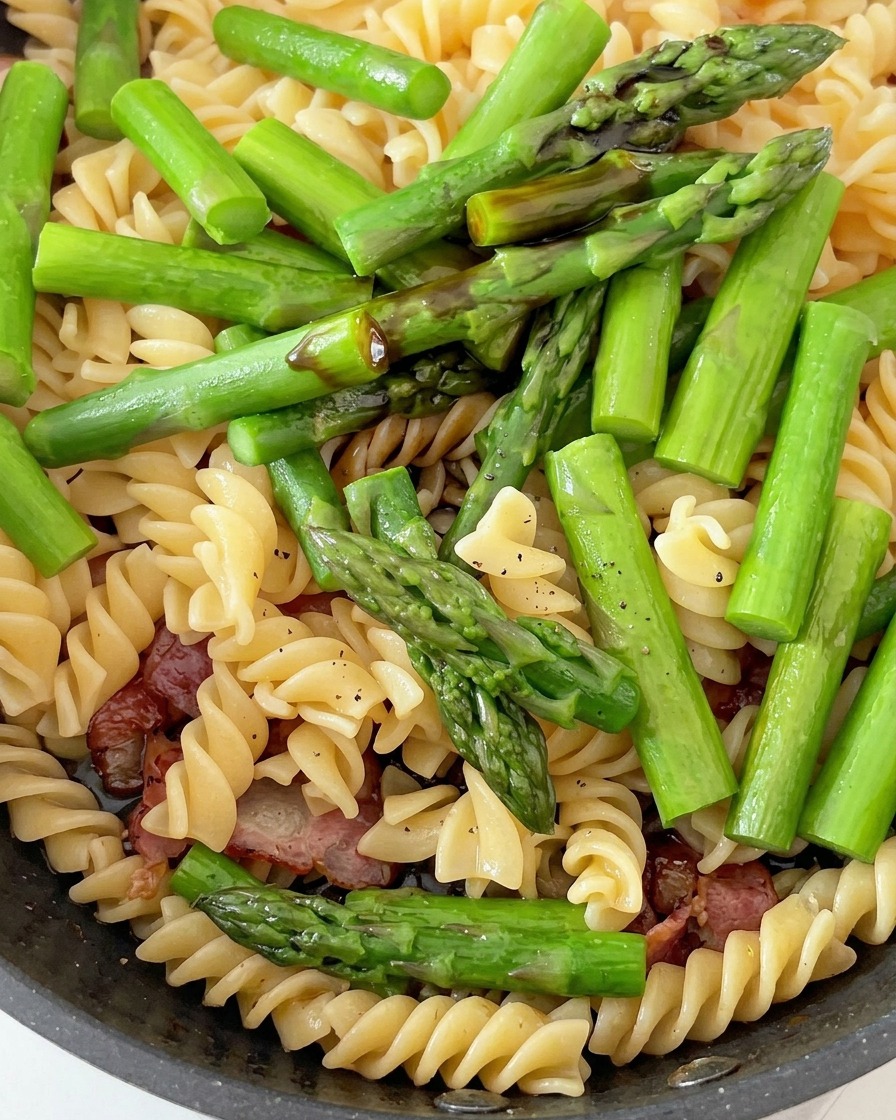 パスタとアスパラ、ベーコンをソースで絡めている様子。