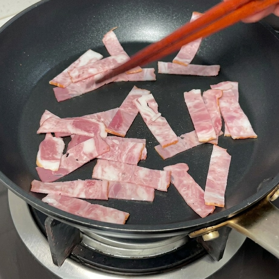 フライパンでベーコンをこんがりと焼いている様子。