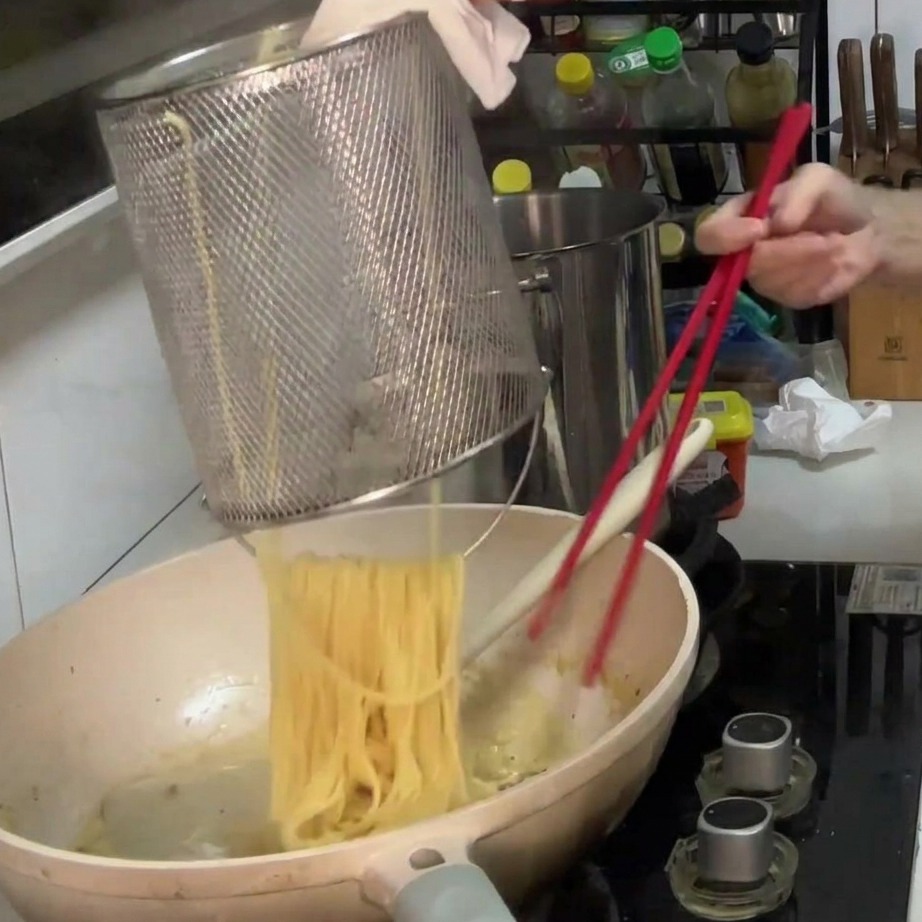 茹で上がったパスタをクリーミーなソースと絡めている様子。