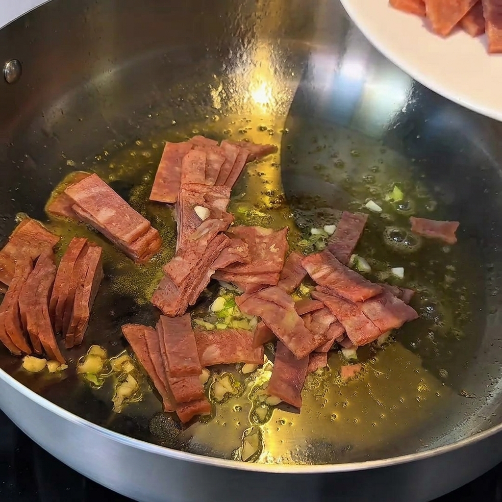 フライパンの中で溶けたバターと一緒ににんにくとベーコンを炒めている様子。