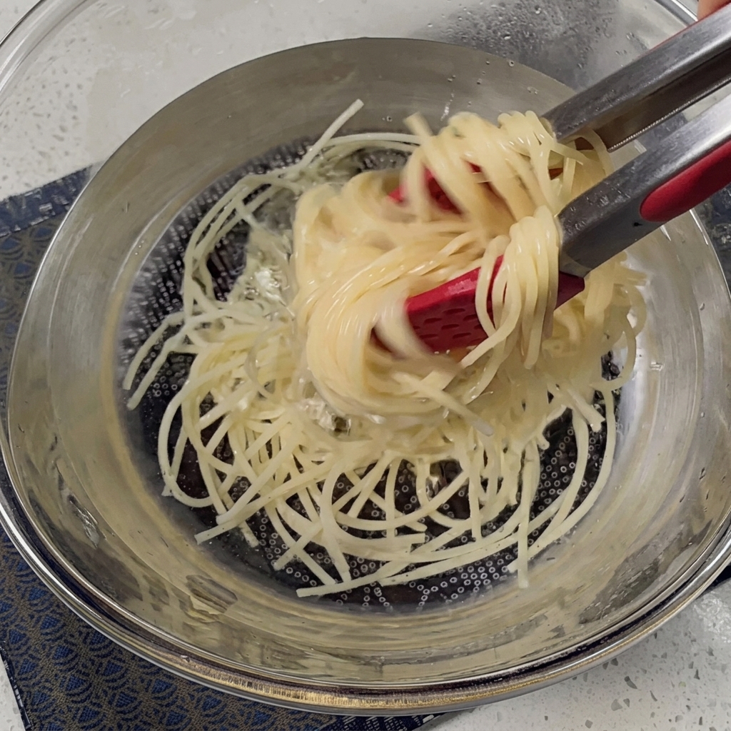 金属製のざるで茹で上がったスパゲッティのお湯を切っている様子。