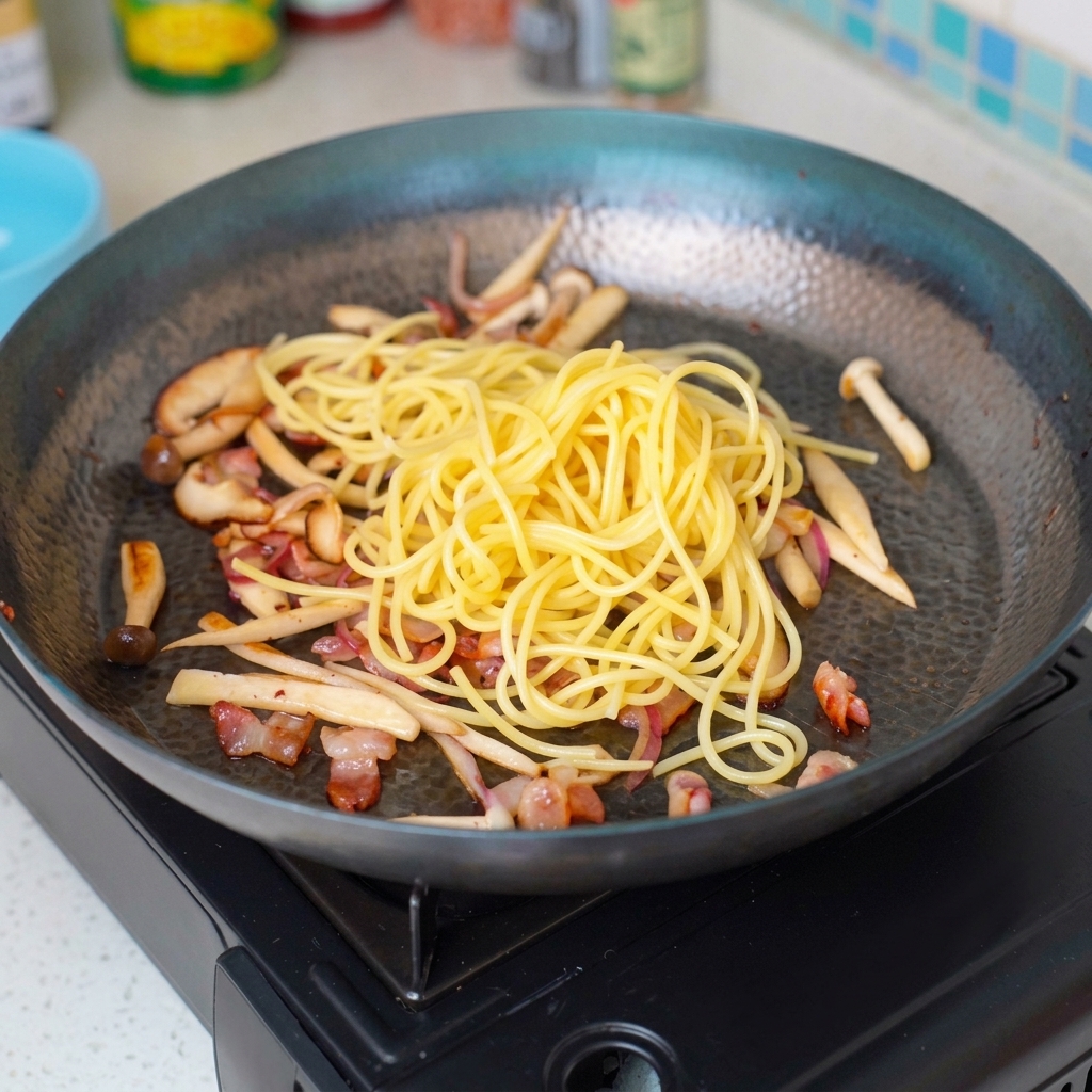 茹で済みのパスタをフライパンに入れ、他の具材と混ぜ合わせている様子