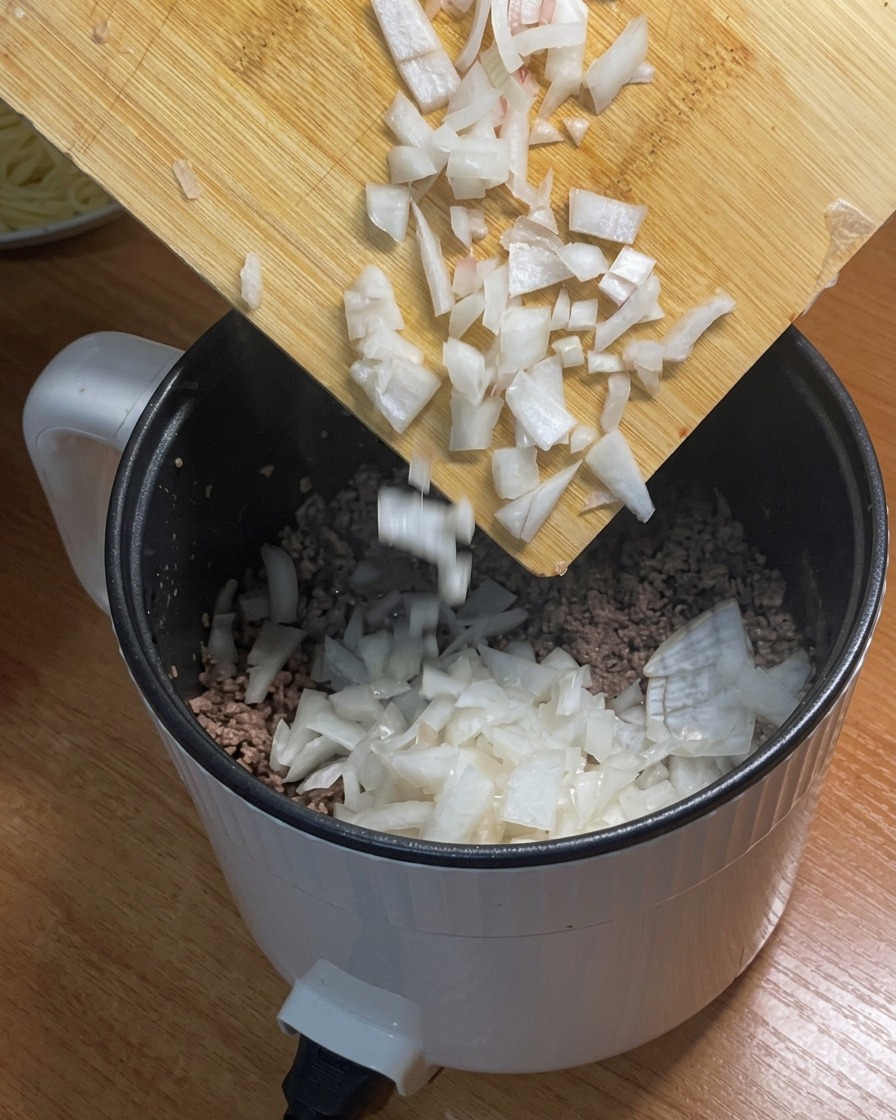 炒めたひき肉に玉ねぎを加える様子