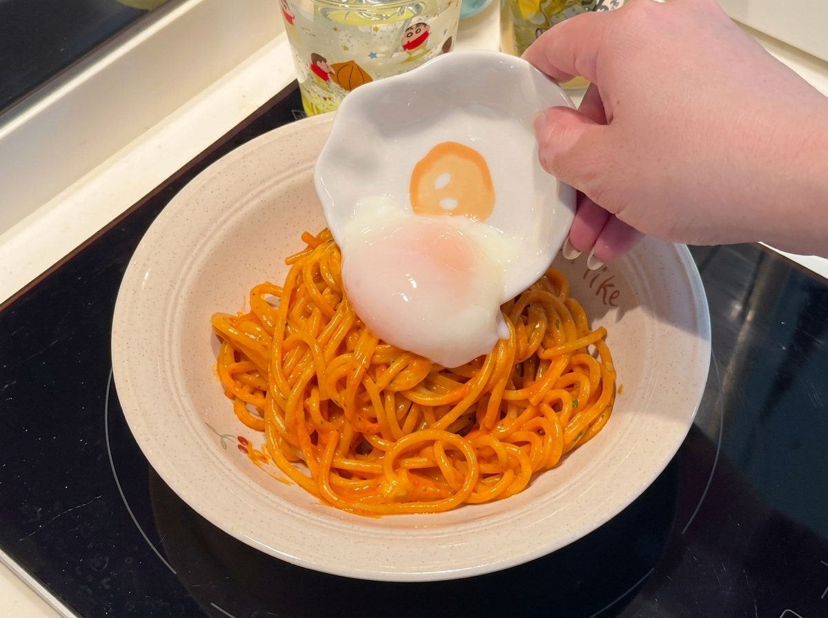 皿に盛られたパスタの中央に半熟卵をのせる様子
