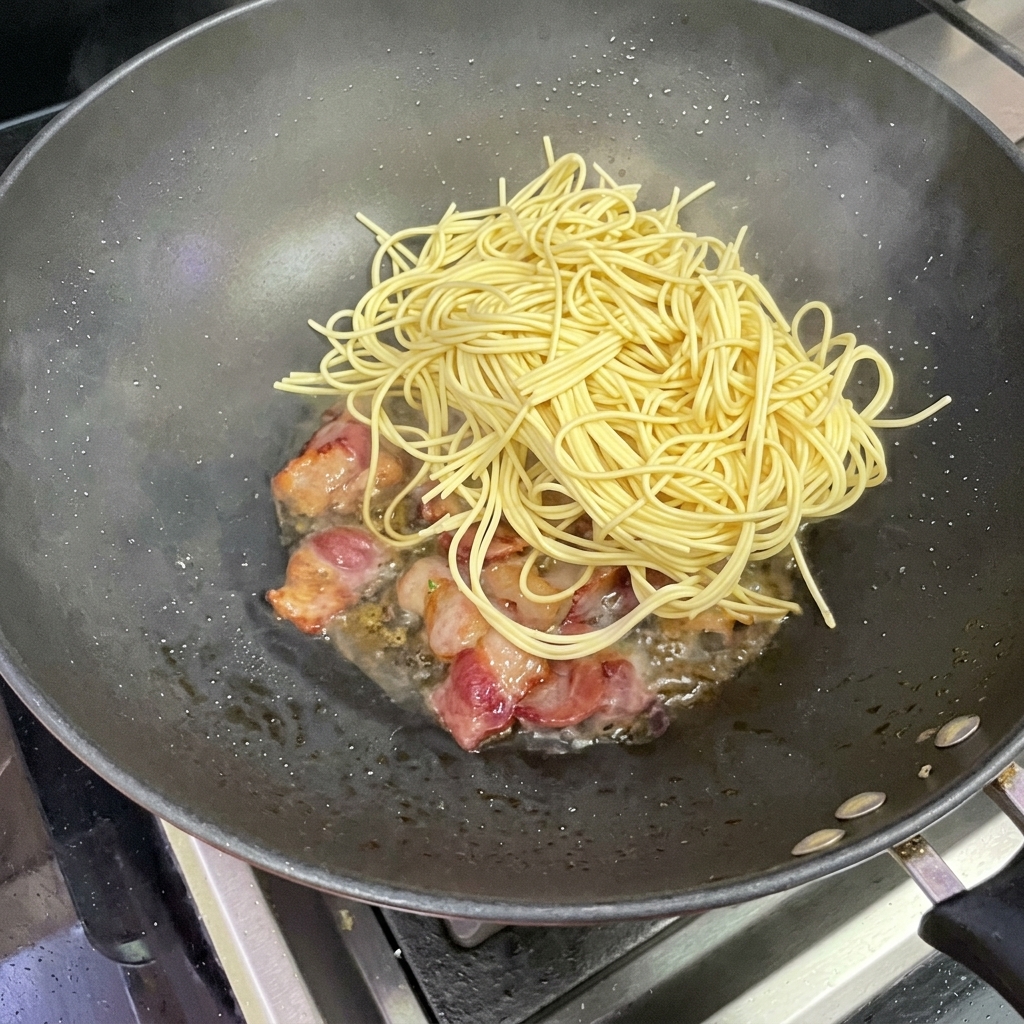 ベーコンの入った中華鍋にスパゲッティを加えている様子。