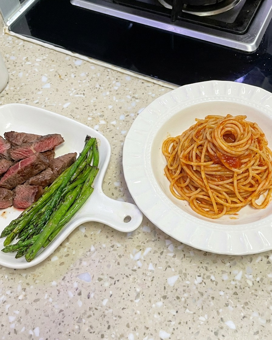 ソースが絡んだスパゲッティをトングで中華鍋から持ち上げ、白いボウルに盛り付けようとしている様子。