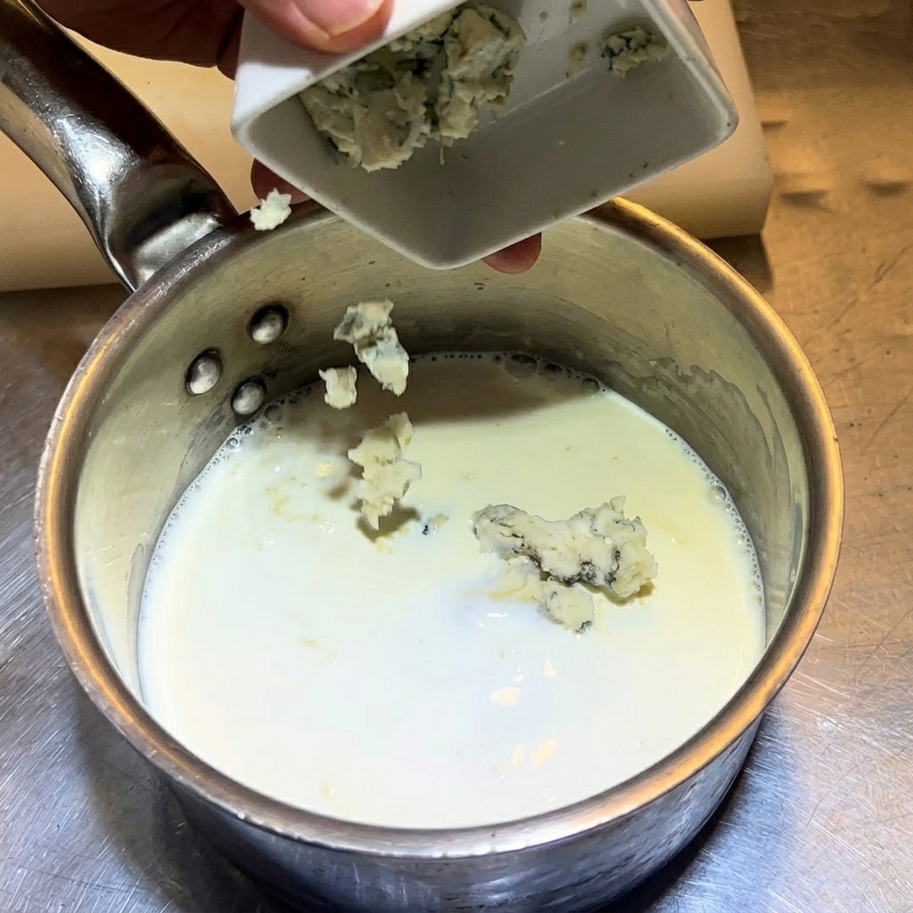 牛乳とクリームの入った鍋に、崩したブルーチーズを入れている様子。
