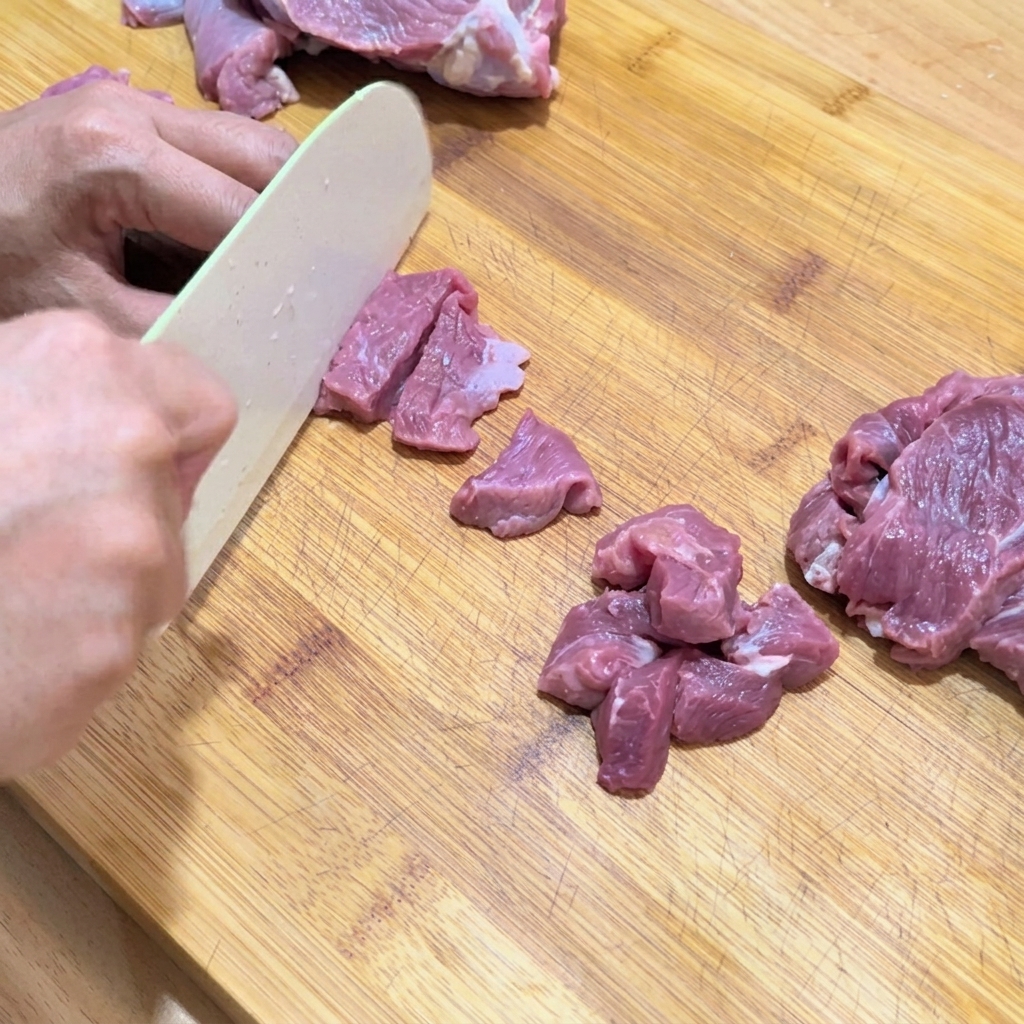 生の牛肉をまな板の上で均等な一口大の角切りにする様子。