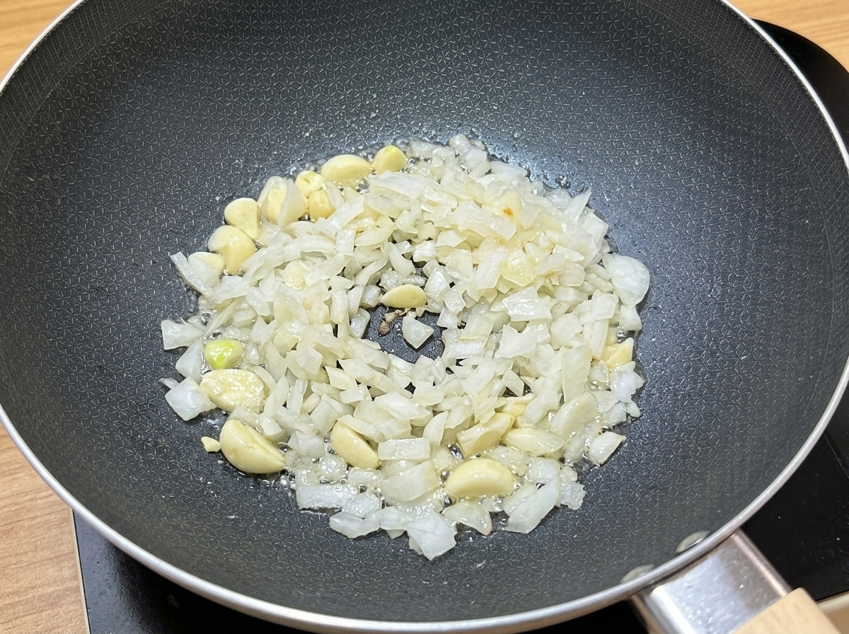 フライパンに油を引き、刻んだにんにくと玉ねぎを炒めている様子。