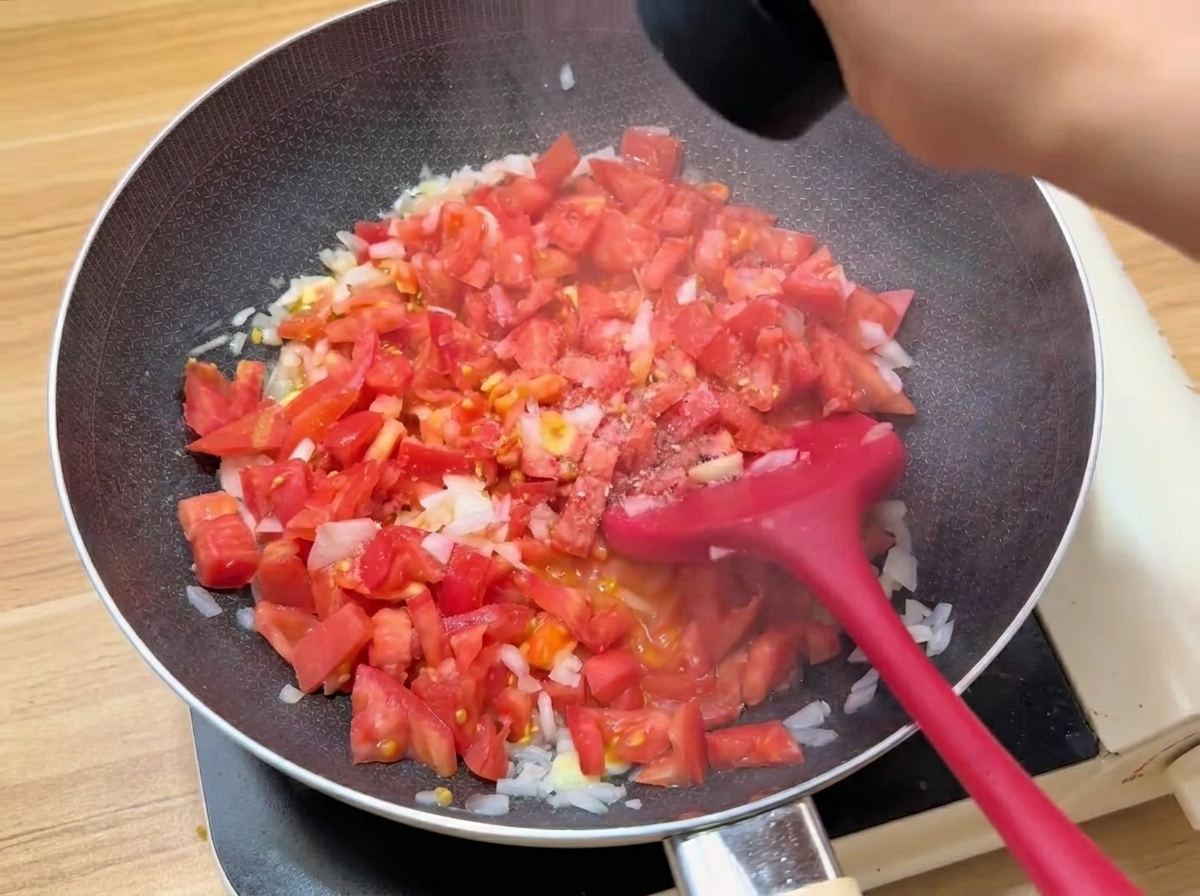 フライパンでトマトを煮詰め、調味料を加えている様子。