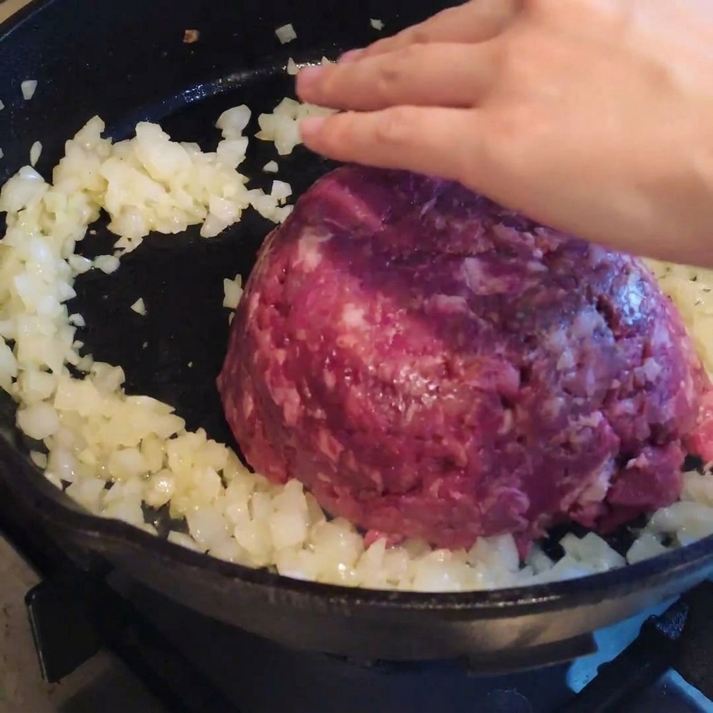 炒めた玉ねぎが入ったフライパンに牛ひき肉を加え、調理している様子。