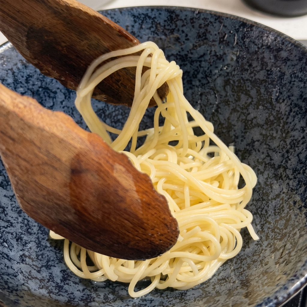 大きな木製のスプーンで茹で上がった麺をすくい上げている様子。