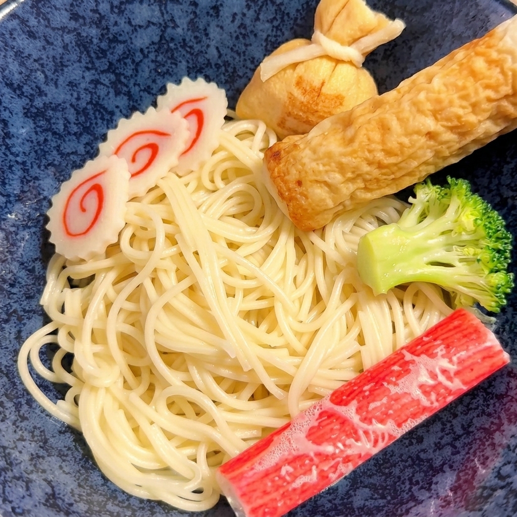 トングを使って、茹でた麺を器の中に盛り付けている様子。