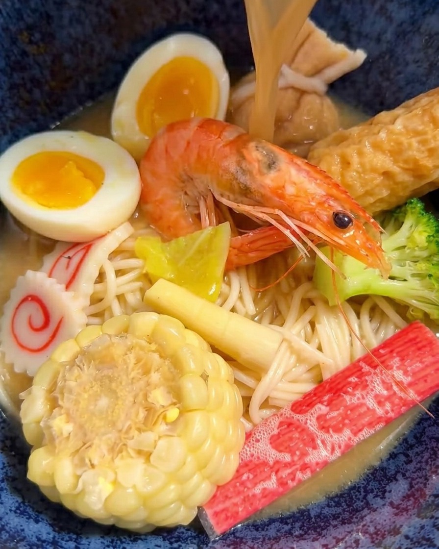 器に入れた麺に、具材を盛り付けて熱い味噌スープを注いでいる様子。
