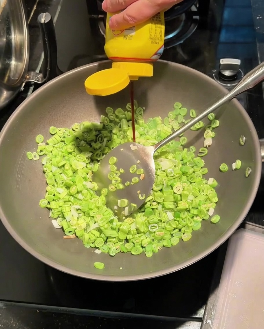 炒めたインゲンに調味液を加えている様子。