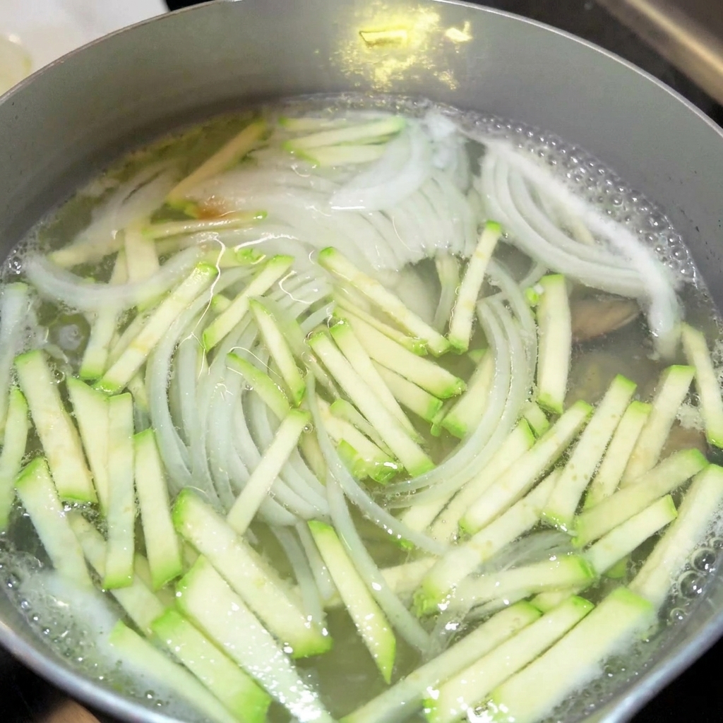 煮立っている野菜スープに醤油やナンプラーを加えている様子。