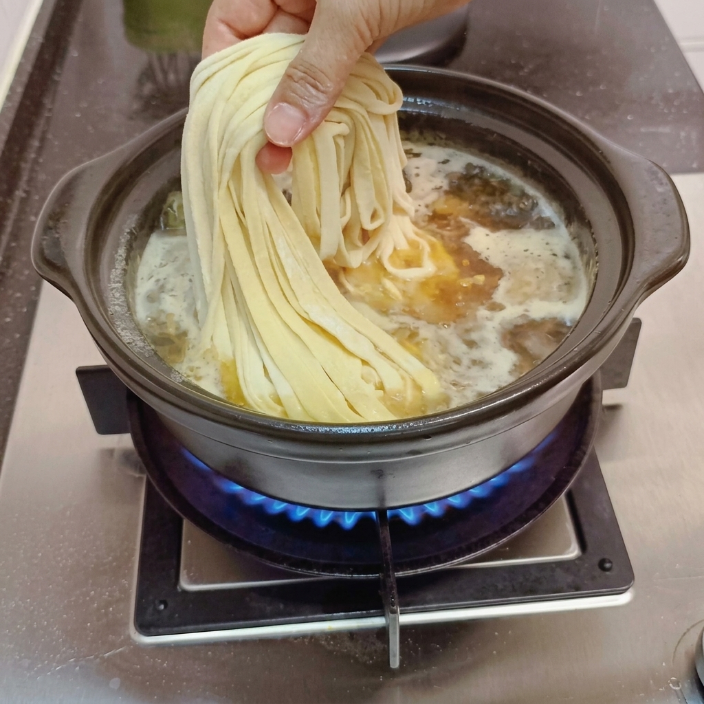沸騰したスープに生麺を入れる様子。
