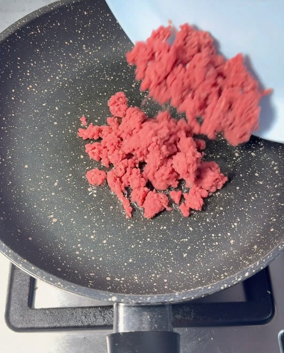 油を引いたフライパンに生の牛ひき肉を入れている様子。