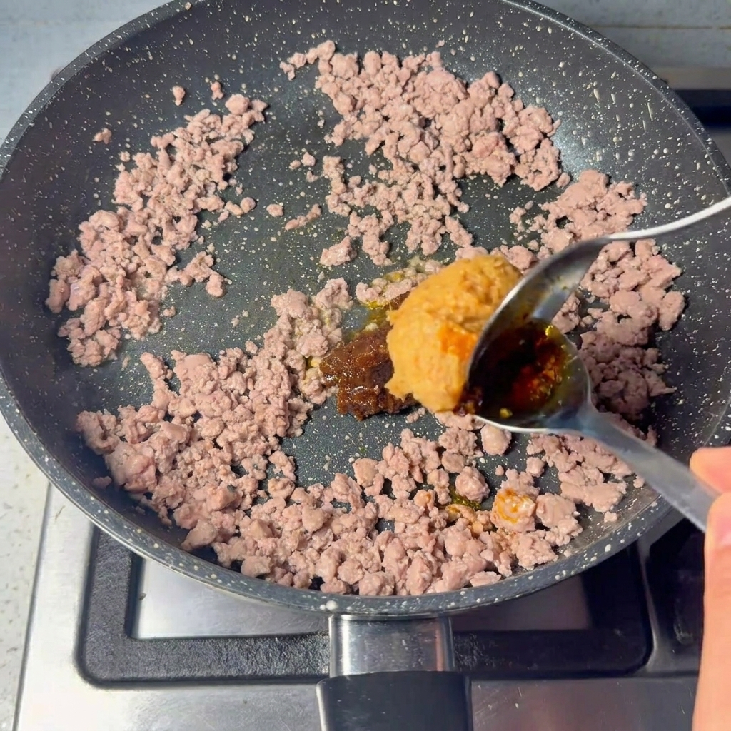 炒めたひき肉にたっぷりのペーストを加えている様子。
