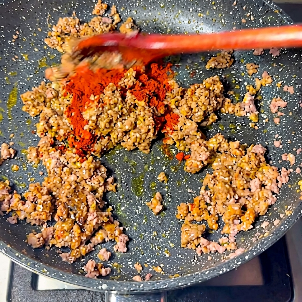 炒めた肉にチリパウダーを振りかけている様子。