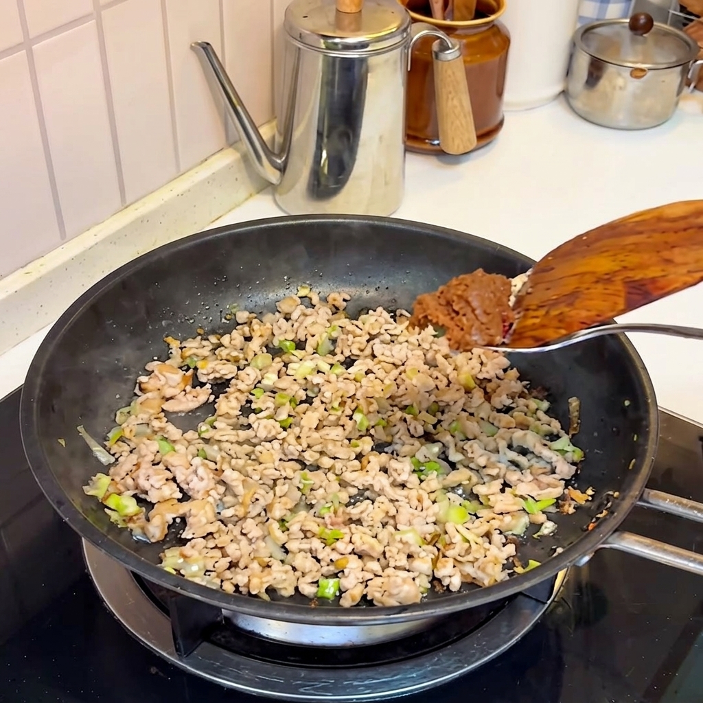 炒めた肉に味噌を加えている様子